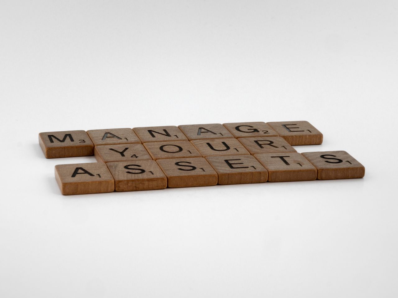 services-02 Wooden Scrabble tiles spelling 'Manage Your Assets' on a white background.