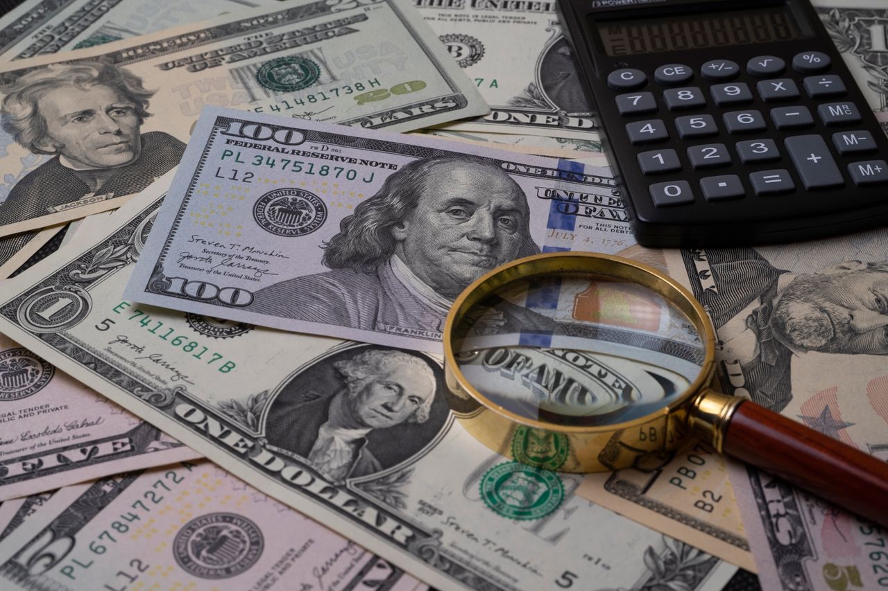 about-us-01 US currency bills with magnifying glass and calculator, symbolizing financial analysis.
