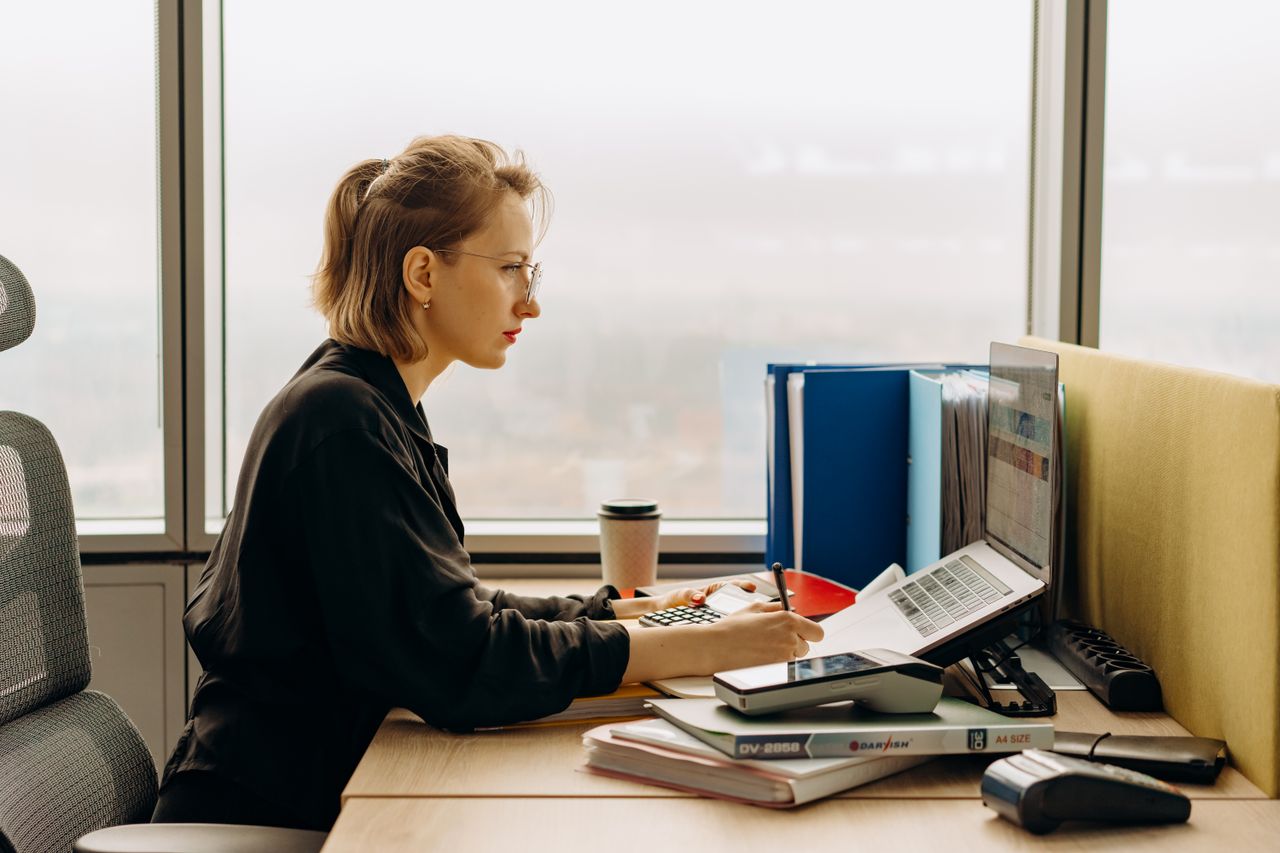 Mastering the First Impression: Your intriguing post title goes here Dedicated woman using laptop and calculator in modern office setting.
